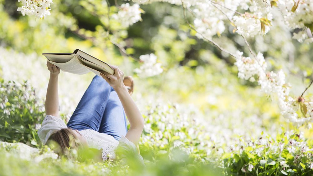 vrouw leest een boek in het gras met bloemen 