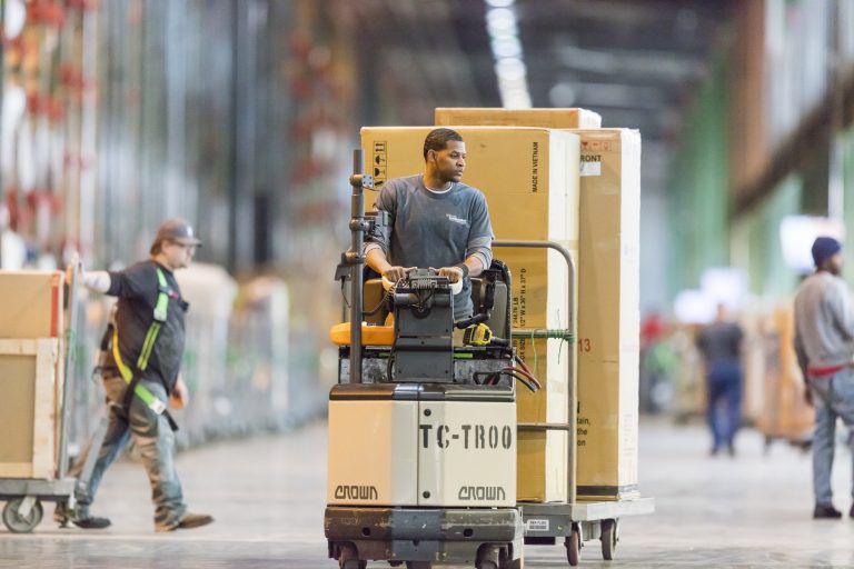 A man driving a pallate stacked with boxes through a warehouse