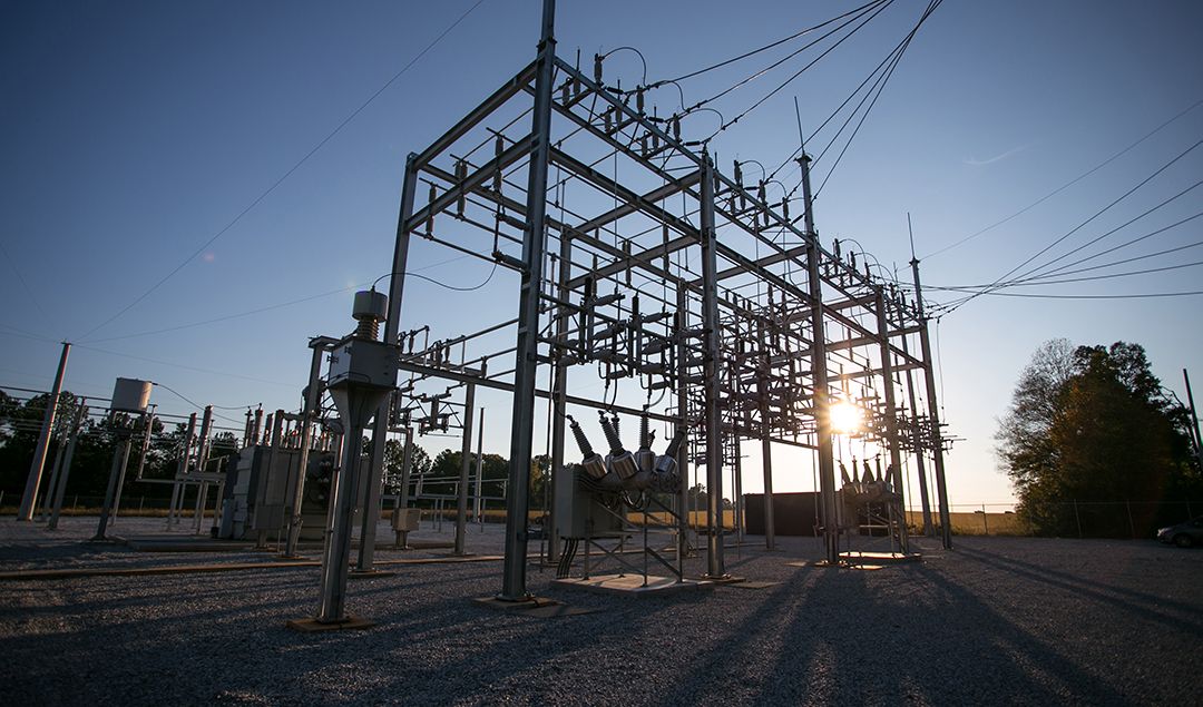 A substation with the sun shining from behind it.