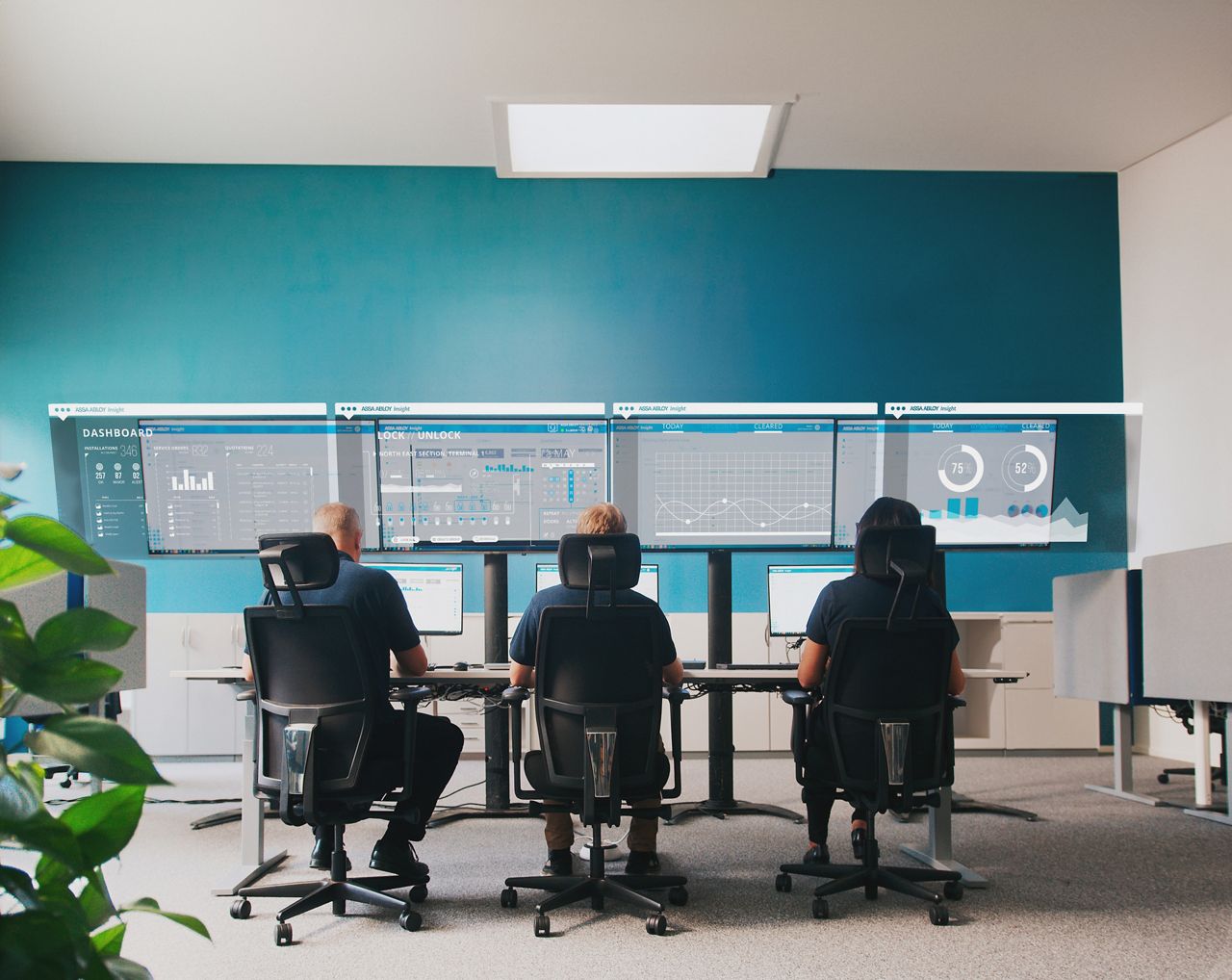 Tři lidé sedící u stolu s monitory