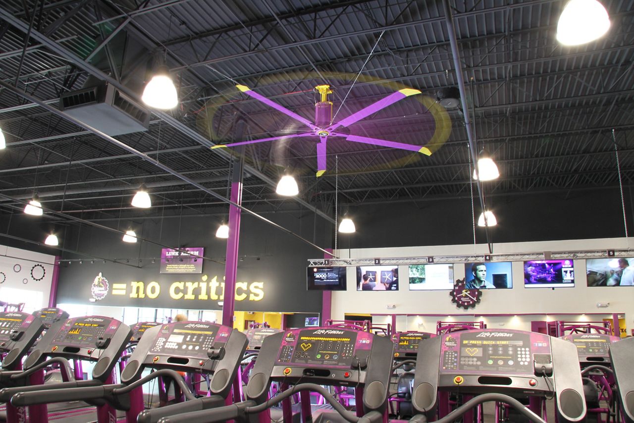 The inside of Planet Fitness filled with exercise machines with a large purple and yellow fan hanging from the ceiling