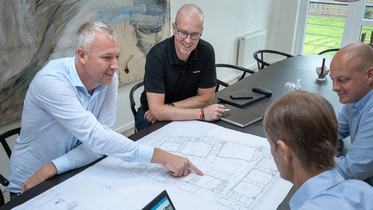 Personer sidder om et bord men en plantegning