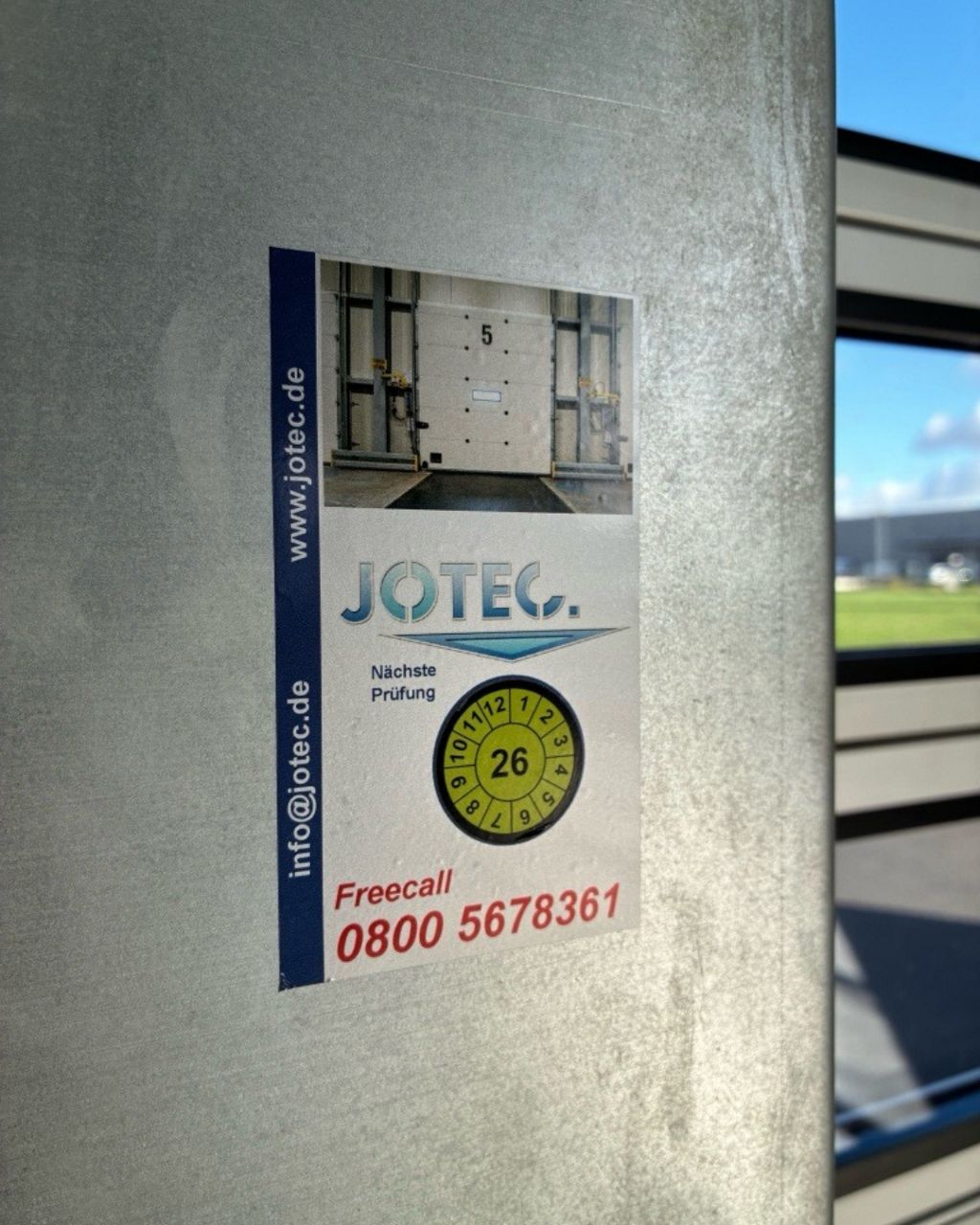 Aufgeklebte Prüfplakette der Firma Jotec über das Prüfjahr 2026 neben einem Schnelllauftor