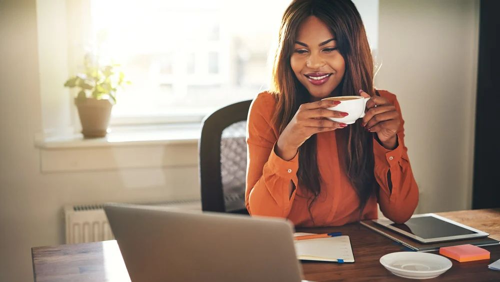 A professional woman multitasking at her desk with a laptop and a cup of coffee.