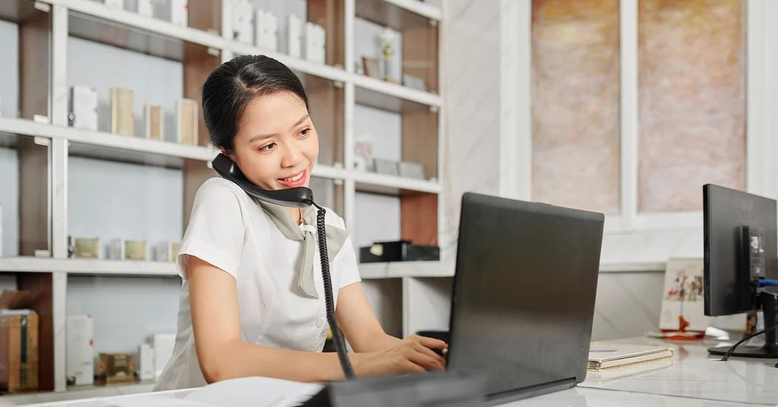 A woman wearing a headset while working on her laptop, engaged in a professional conversation.