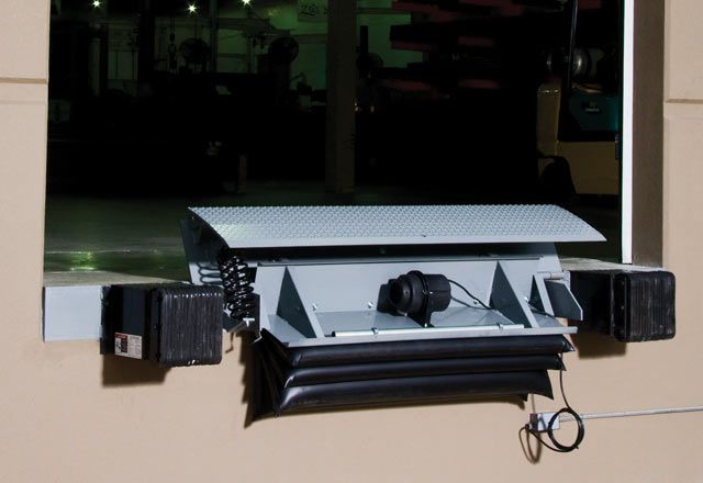 A silver edge of dock leveler attached outside of a warehouse.