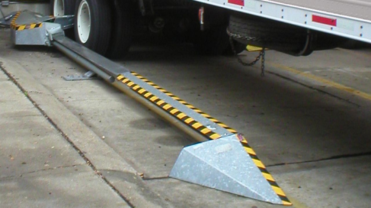 A surface-mounted device engineered for dependable wheel restraint and vehicle safety with half of a trailer in view. 