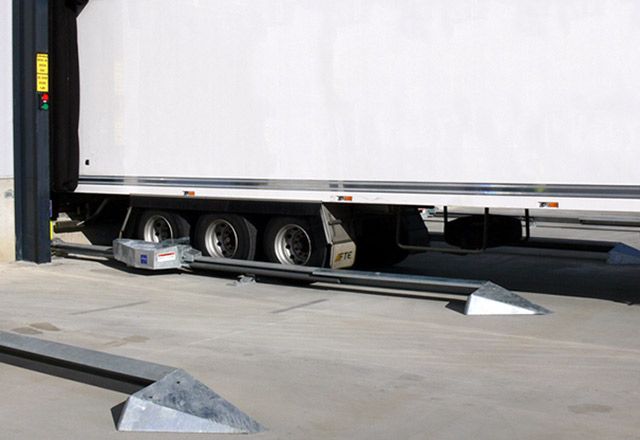 Image: The SLSC Mounted Wheel Restraint under a white truck outside of a warehouse.