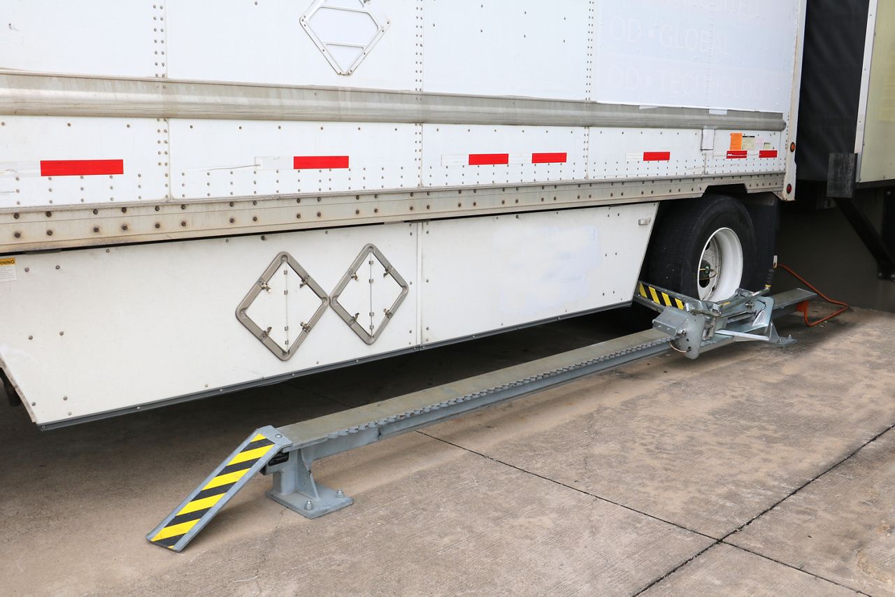 Image: Side view of the SMWC Series Manual Chock Wheel Restraint in use under a white truck.