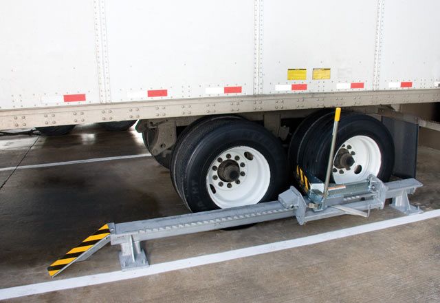 The SMWC Series Manual Chock Wheel Restraint in use under a white truck.