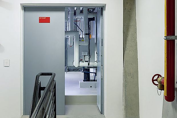 Einflügelig geöffnete Tür in einem Treppenhaus zu einem Raum mit Rohren