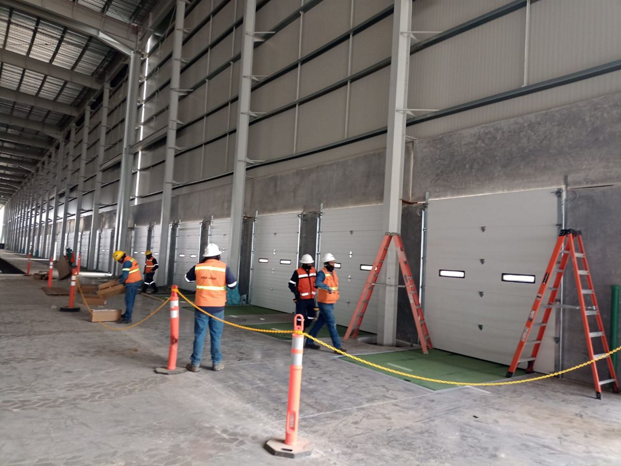 Dos hombres estrechan sus manos frente a una puerta seccional, uno lleva una chaqueta ASSA ABLOY.