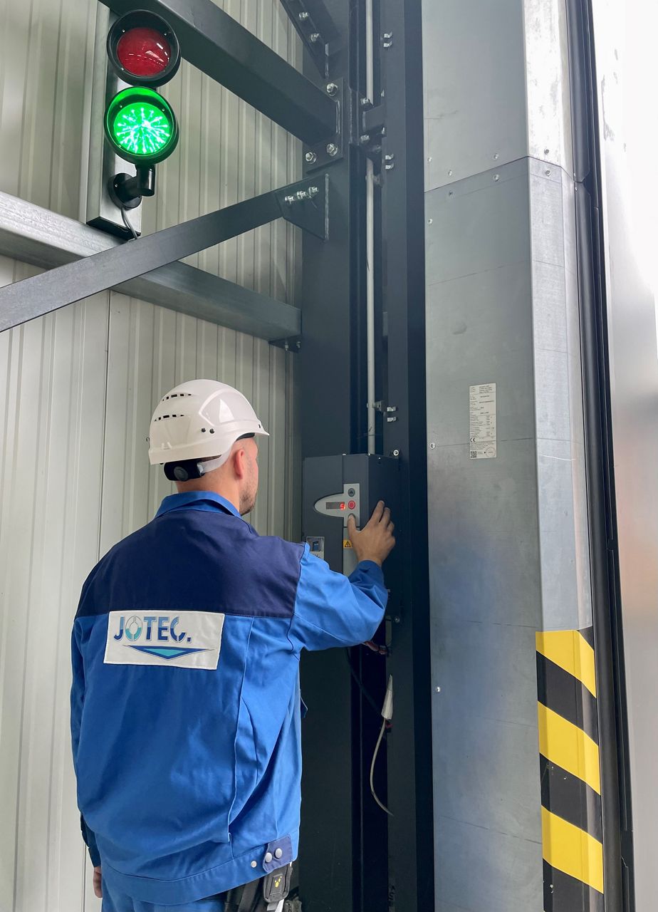Techniker mit Jotec-Logo auf dem Rücken und einem Helm steht vor einer Torsteuerung