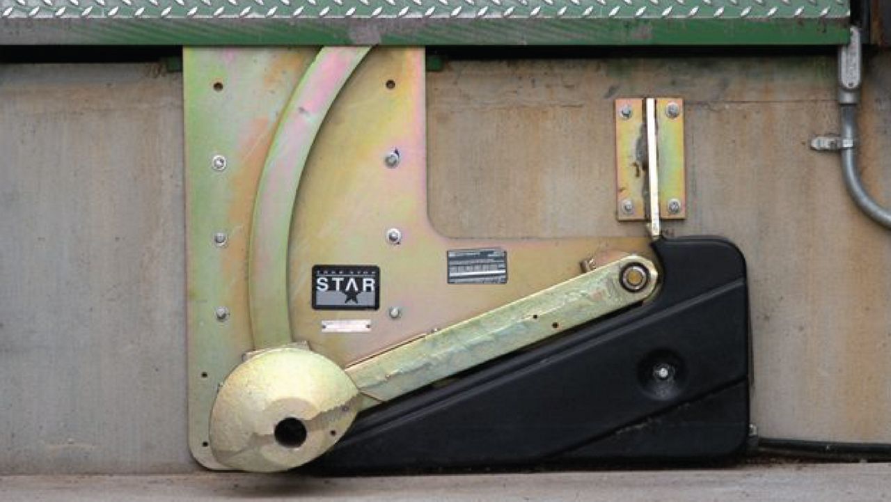 A robust gold-colored industrial device with an enhanced design, featuring a curved restraining arm and visible safety labels.