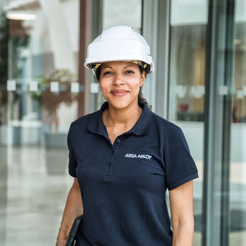 A smiling woman with an ASSA ABLOY branded sweater and a white safety helmet.