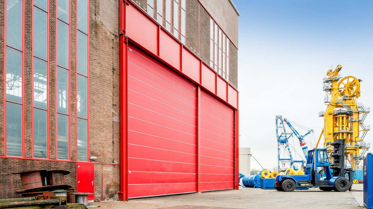 Un bâtiment en briques avec des Megadoor rouges dans un environnement industriel.