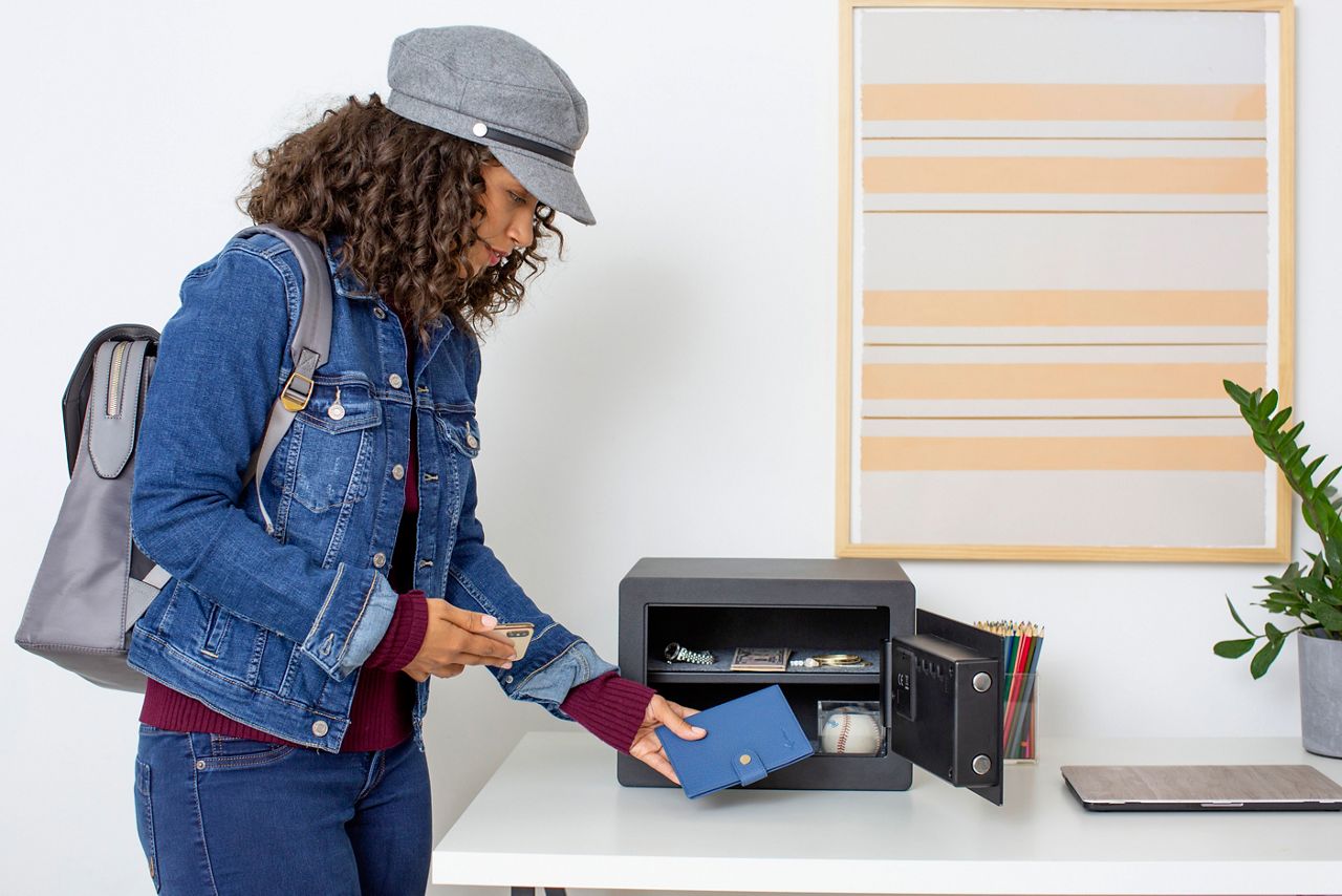 woman is storing away her vauables such as passport and jewlery inside the Yale Smart safe 
