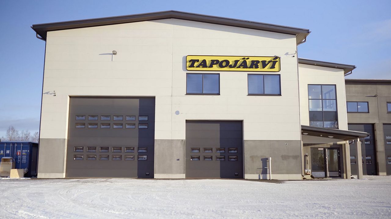 Industrial building with one large and one smaller sectional door side by side, with a prominent Tapojärvi logo mounted on the wall above them