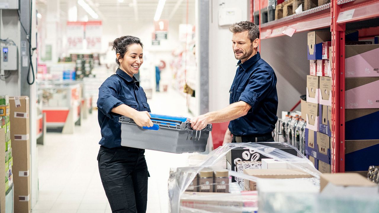 Two coworkers helping out at a grocery store warehouse. 