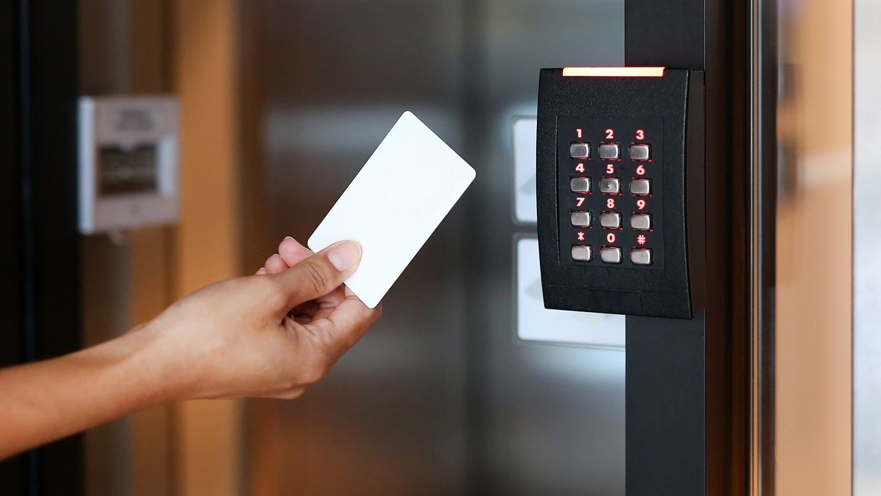 Personne tenant un badge d’accès devant un lecteur de badges avec clavier.