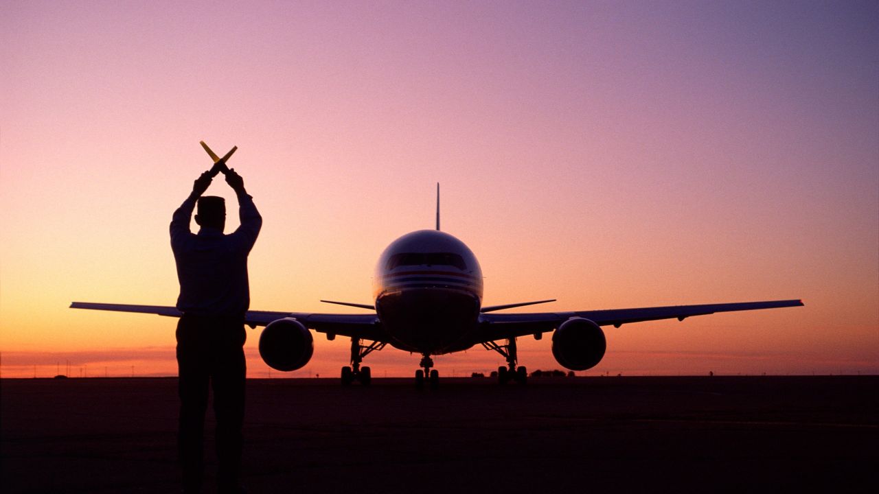 Flyplass ved solnedgang med person som lager signaler med lys i forgrunnen.