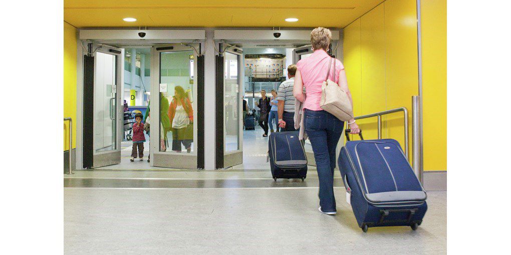automatic swing door at airport exit, with people walking with suitcases