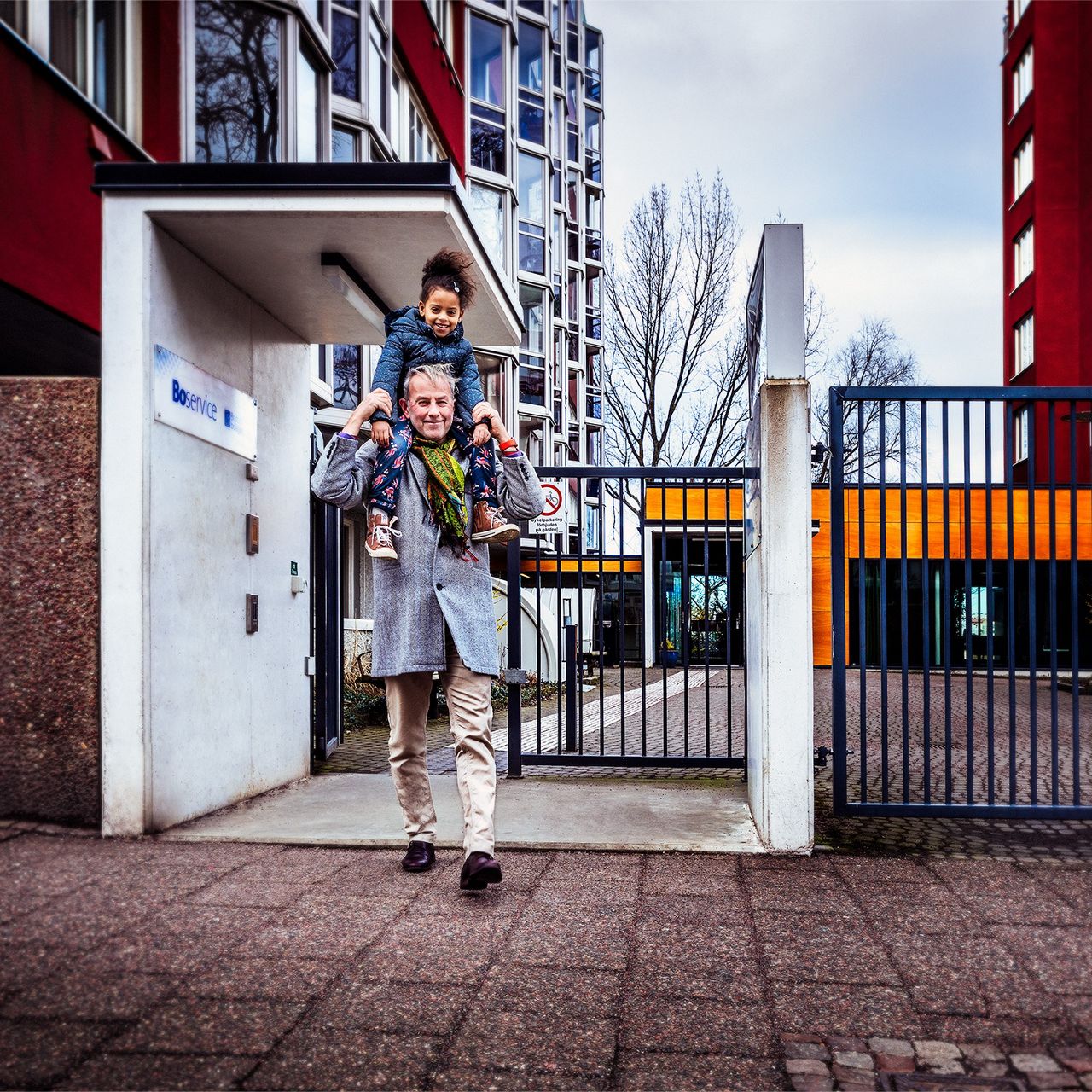 You carry a small child on your shoulders with residential houses in the background.