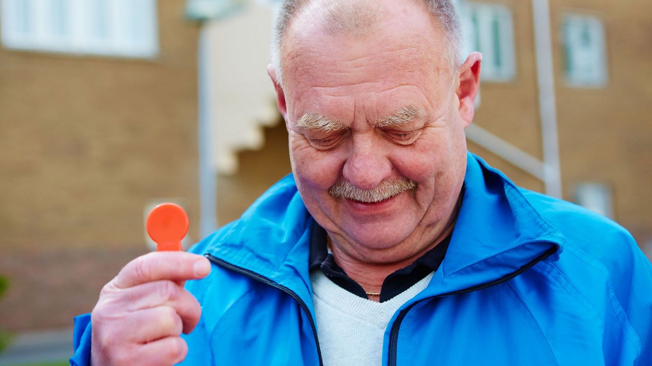 Older man in blue jacket holding an Aptus key.