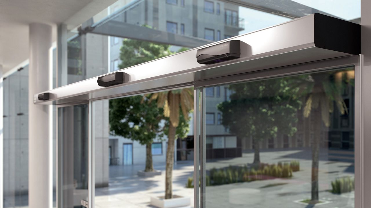 Zbliżenie automatu ASSA ABLOY SL500 na przeszklonych drzwiach przesuwnych.