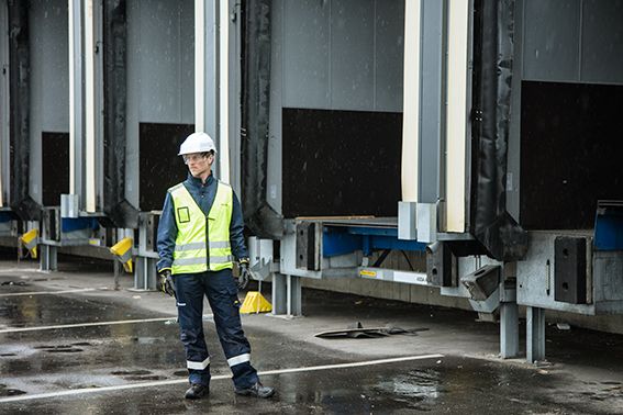 Man met een veiligheidsvest en witte helm staat voor een laadperron met dock levellers en andere laadvoorzieningen.