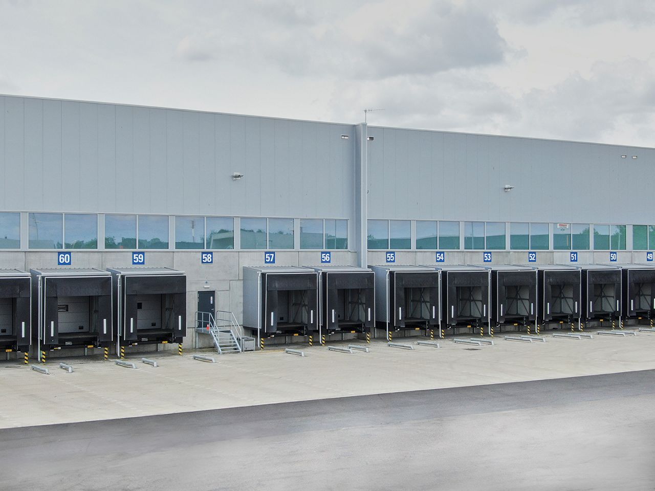Rangée de quais de chargement dans le centre de distribution, numérotés de 54 à 60. Vous y verrez des niveleurs de quai, des sas d'étanchéité et d'autres équipements de chargement et de déchargement d'ASSA ABLOY.