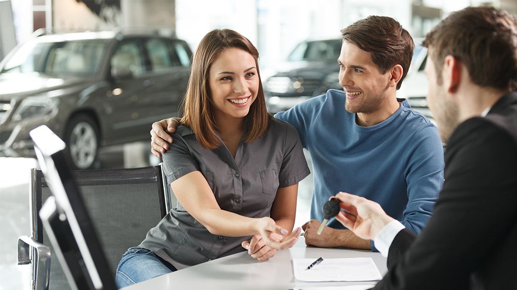 A couple being handed new car keys in an automotive dealership.