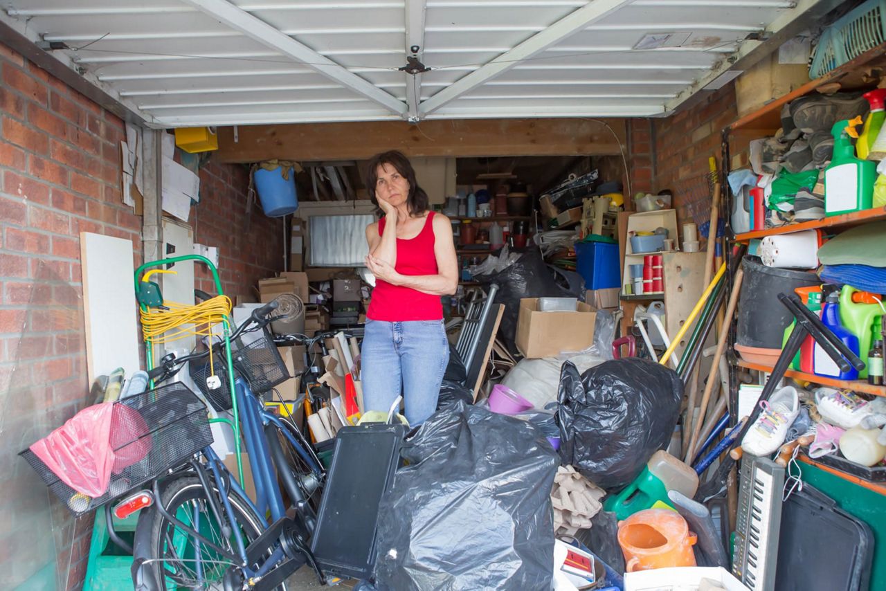 Frustrated woman standing in a messy garage wondering how to start getting an organized garage