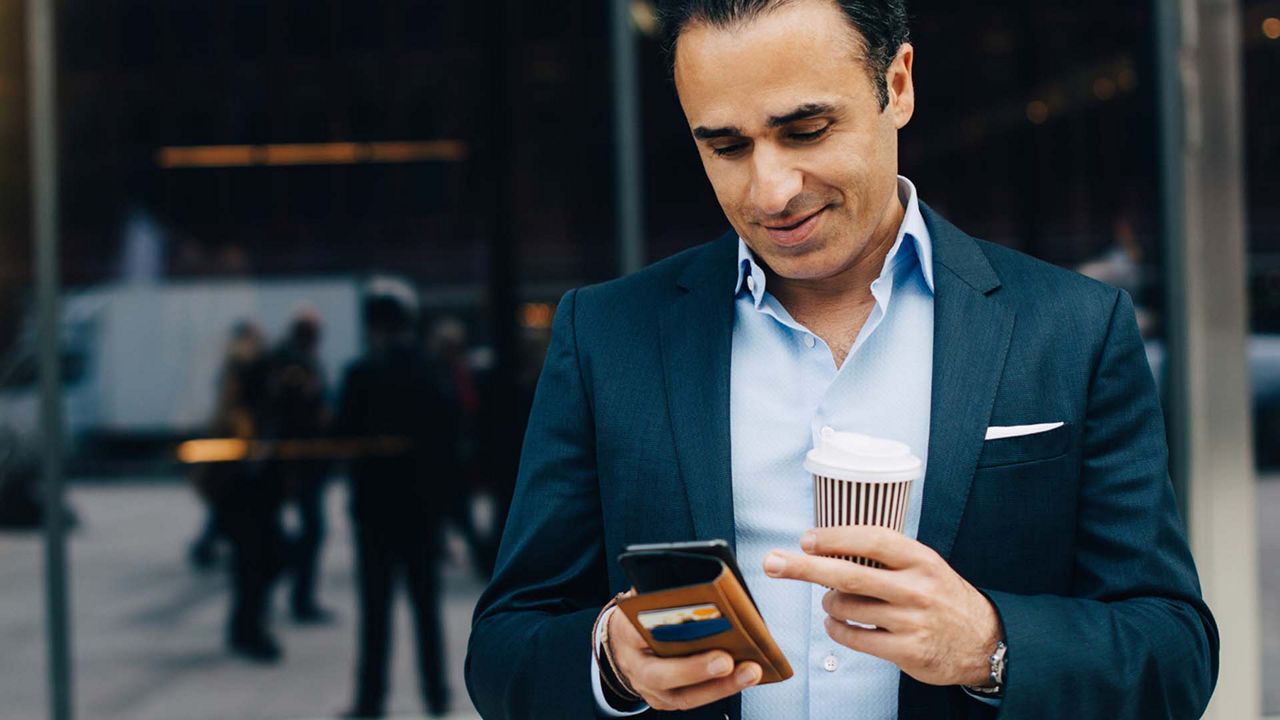 A hand holding a phone, and below is a coffee cup and a news paper. 