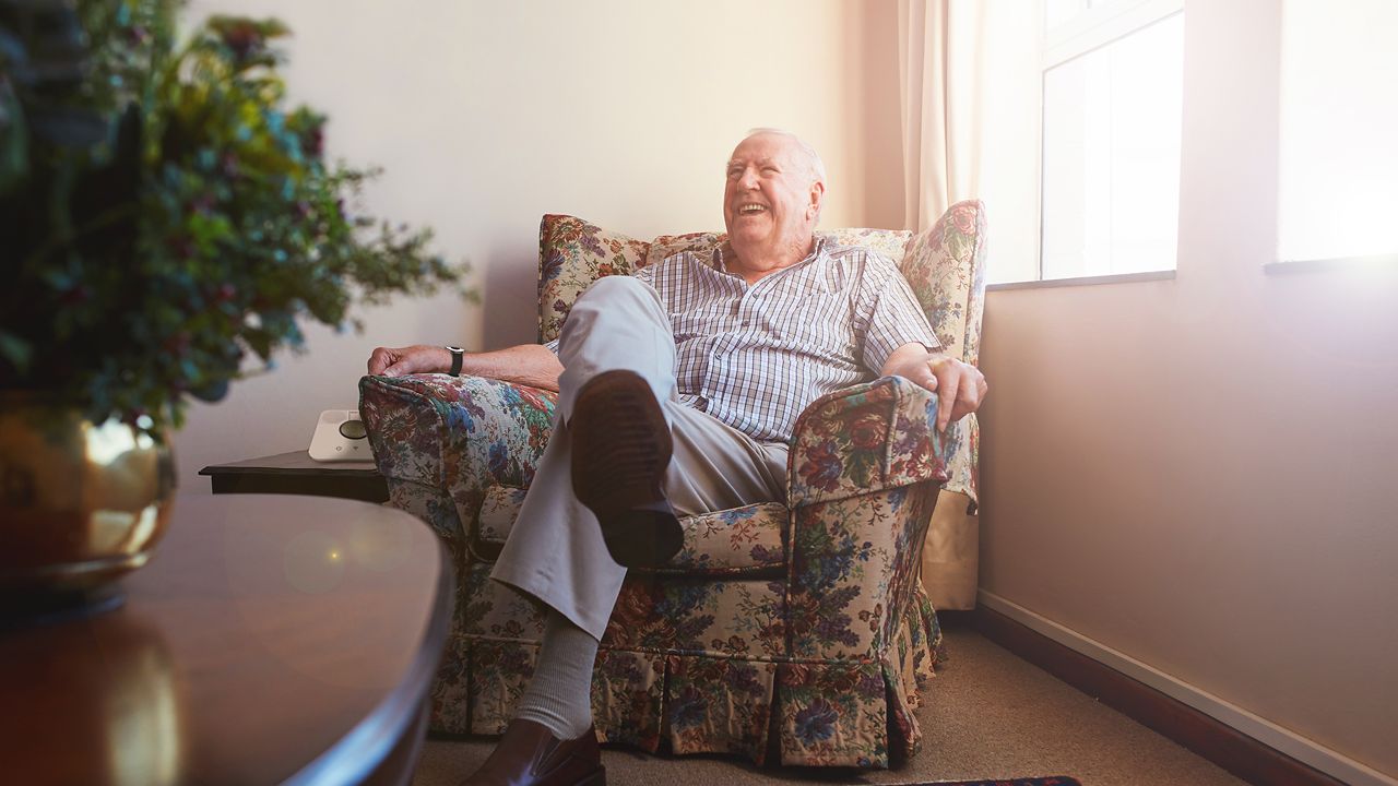Lachende oudere man zit in een fauteuil.