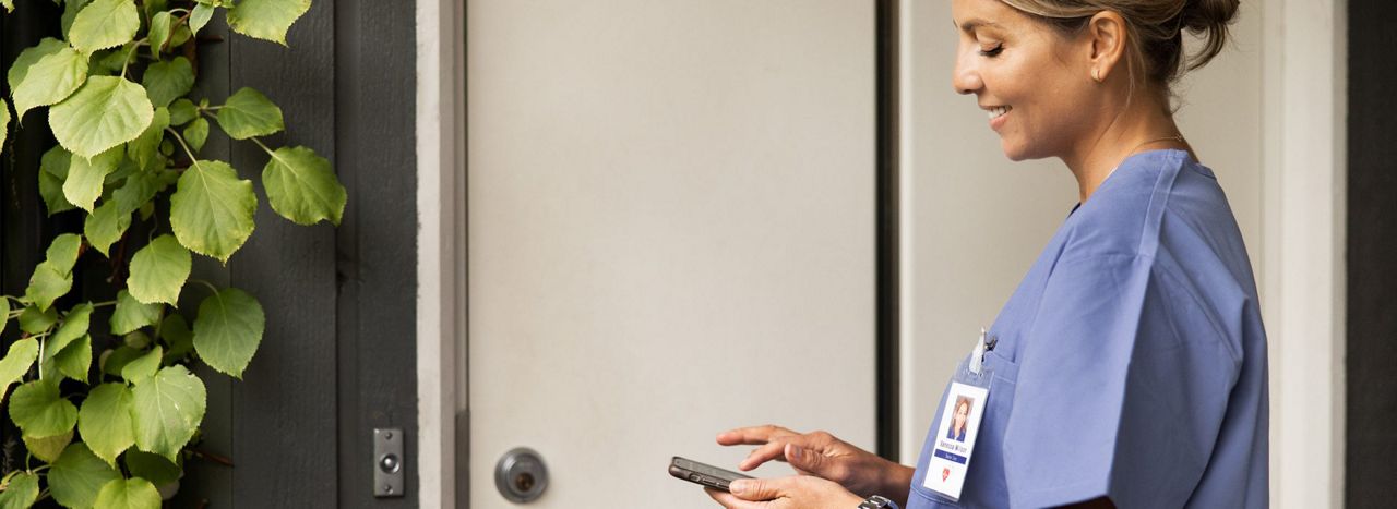 Vrouwelijke thuiszorgmedewerker opent een woningdeur met een app op haar mobiele telefoon.