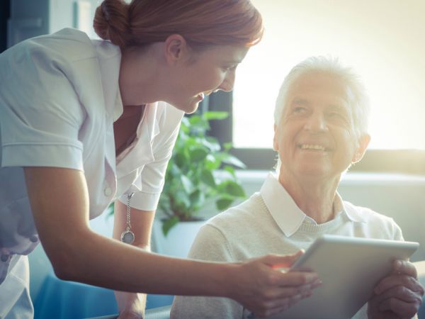 Verpleegkundige en oudere man kijken naar een digitale tablet.