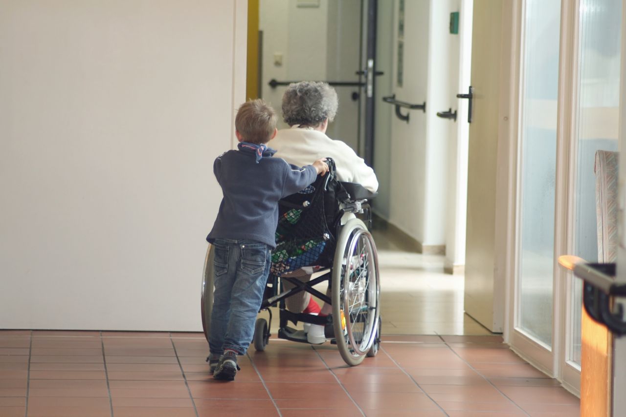 Barn som hjälper mormor i rullstol att gå framåt.