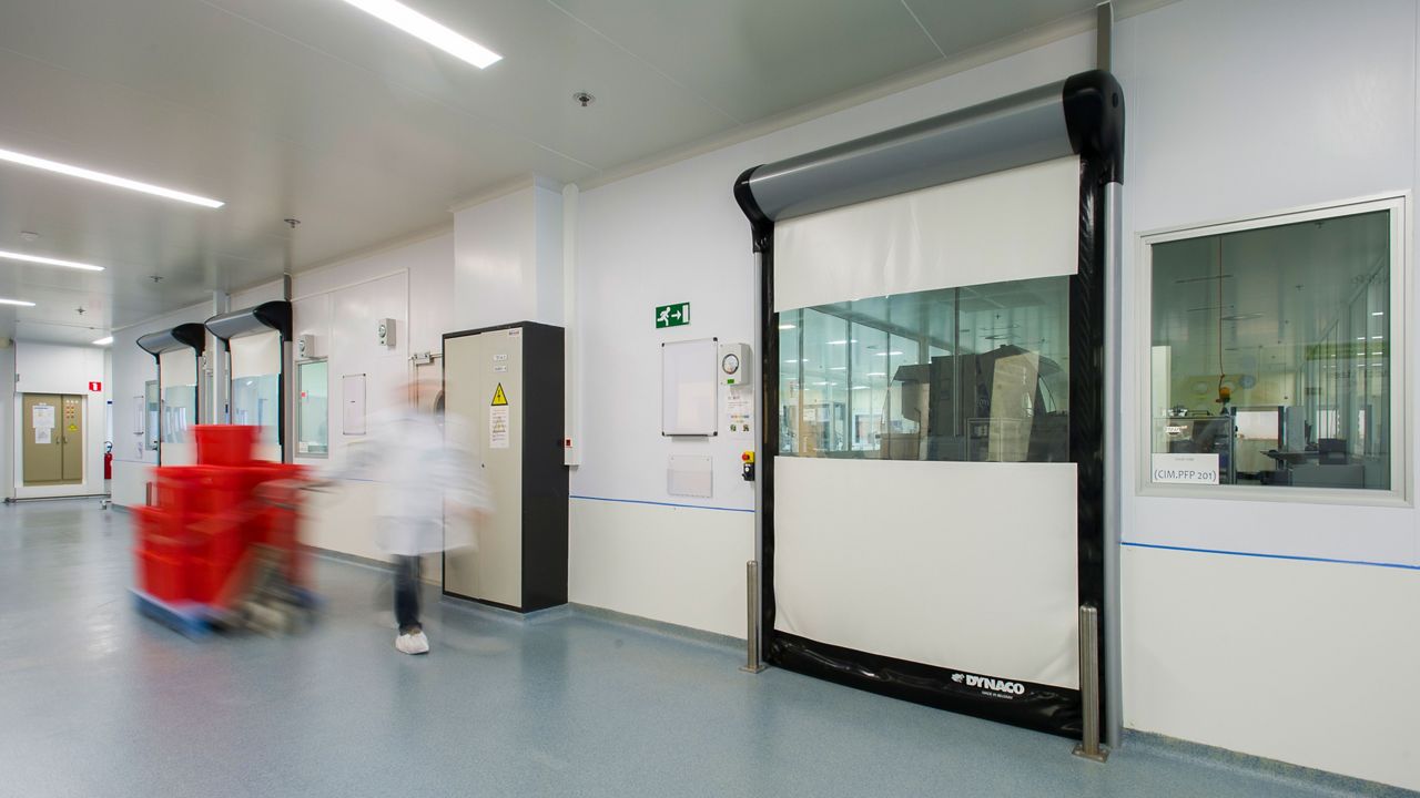 White high-speed doors in a cleanroom with a person walking with red boxes. 