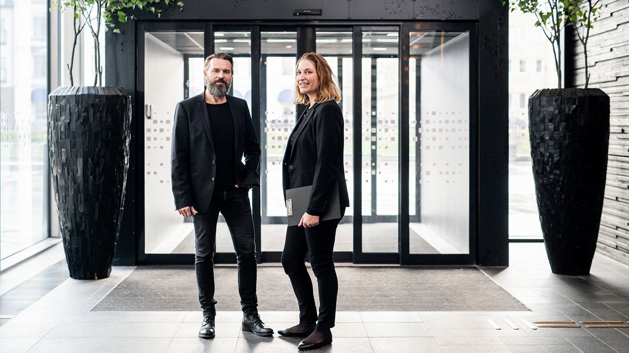 Two people in black clothes standing infront of a glass sliding door.