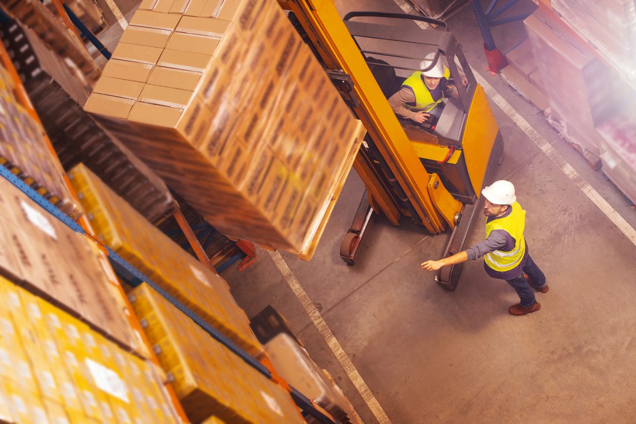 Warehouse workers operating a forklift moving pallets in a distribution and logistics centre