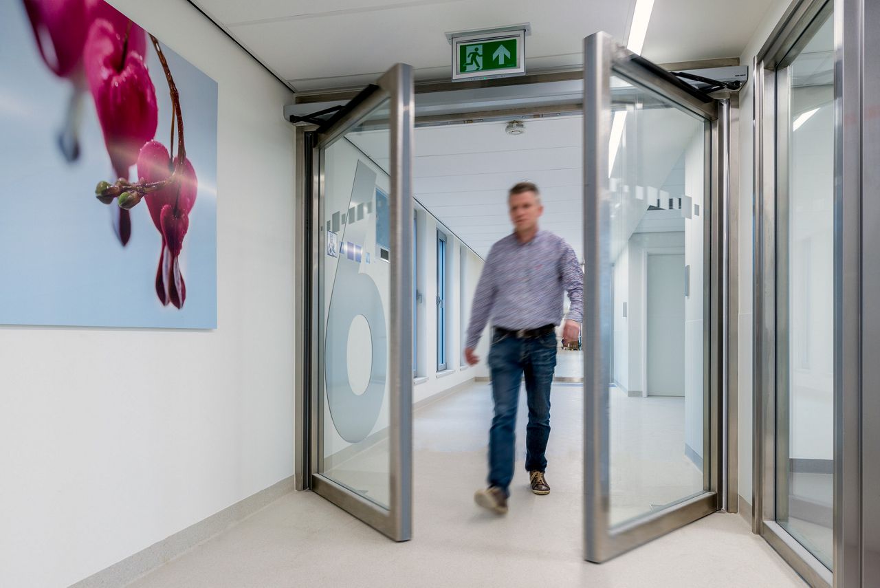 Man loopt door dubbele glazen deuren die naar buiten toe opengaan met een draaideurautomaat