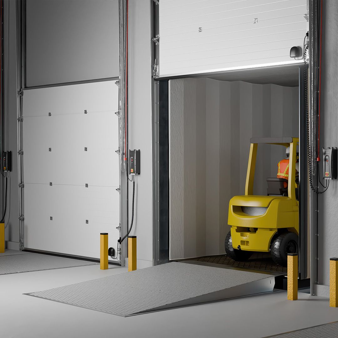 Image: Zonă interioară de încărcare cu o ușă secțională albă ridicată și un stivuitor galben pe rampă, pregătit să intre sau să iasă.