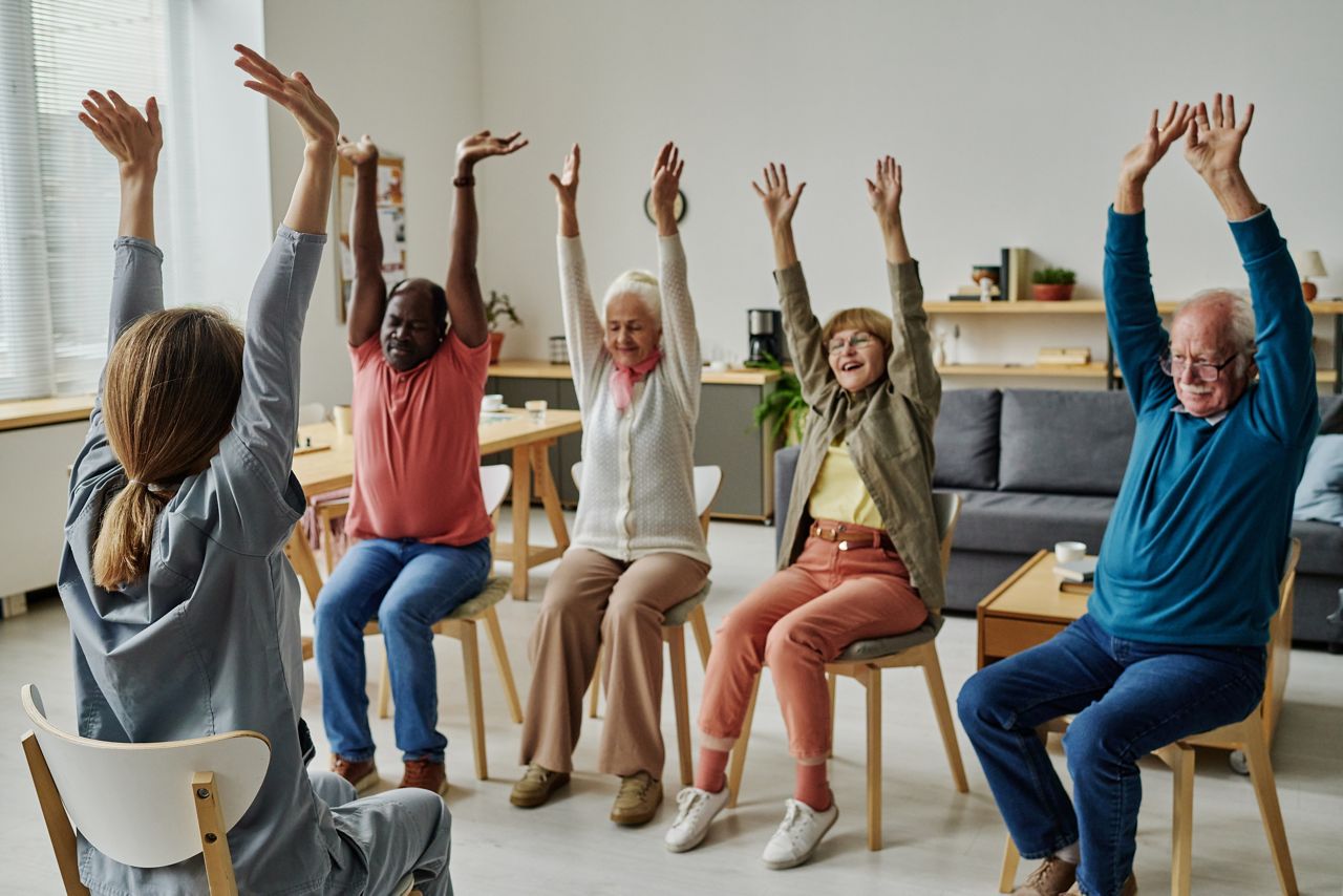 Group of seniors raing their hands in a streching session at a care home.