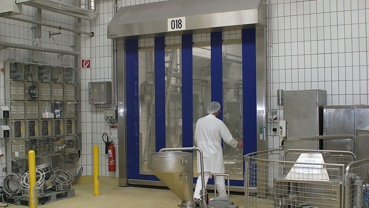 Food industry staff in white protection clothes walking in front of food processing doors.