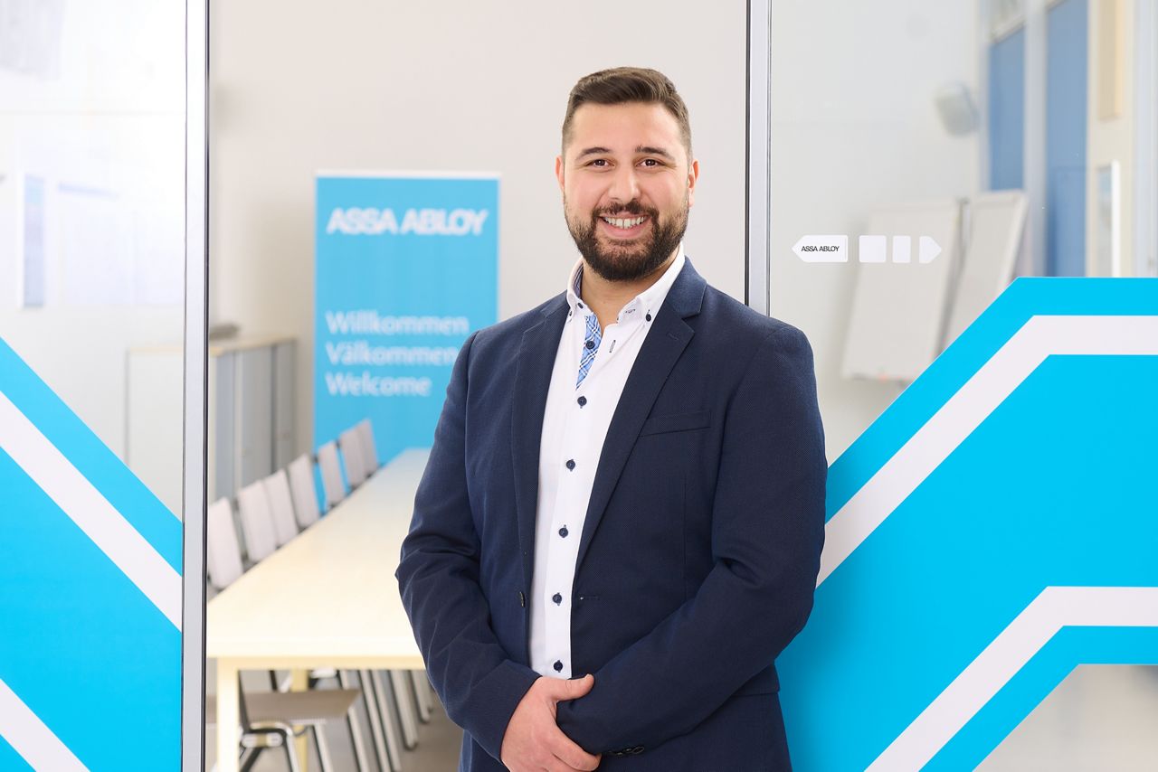 Vertriebsexperte Ihsan Caliskan steht vor einer ASSA ABLOY-Schiebetür mit blauem Hintergrund