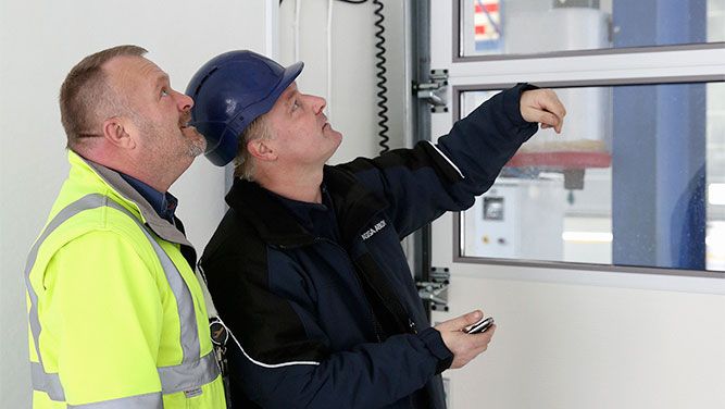 2 mannen met veiligheidskledij bekijken een sectionale poorten met raampjes van ASSA ABLOY