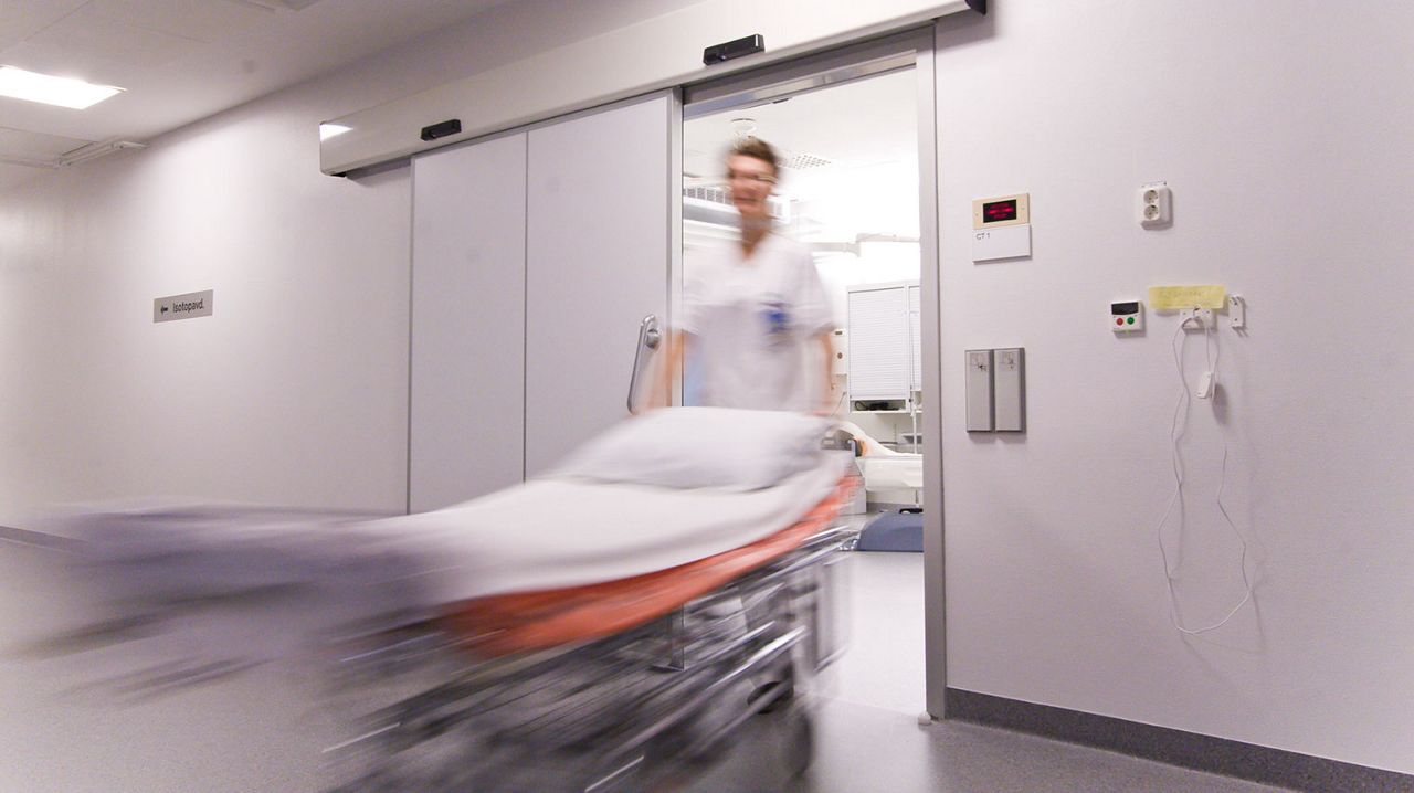 A nurse walking through a sliding door at a hospital with an empty hospital bed. 