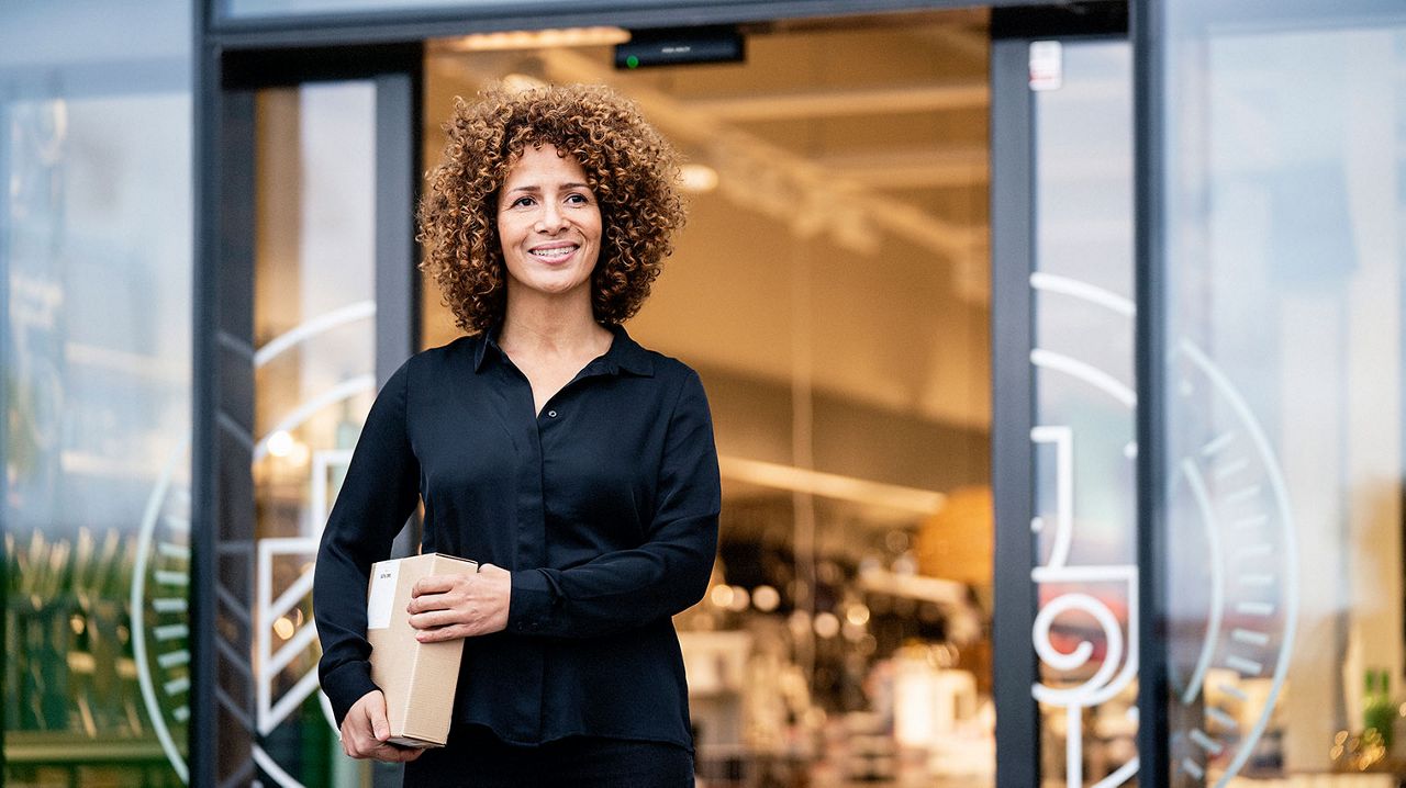 Une femme qui porte un colis sort d’un magasin par des portes coulissantes.