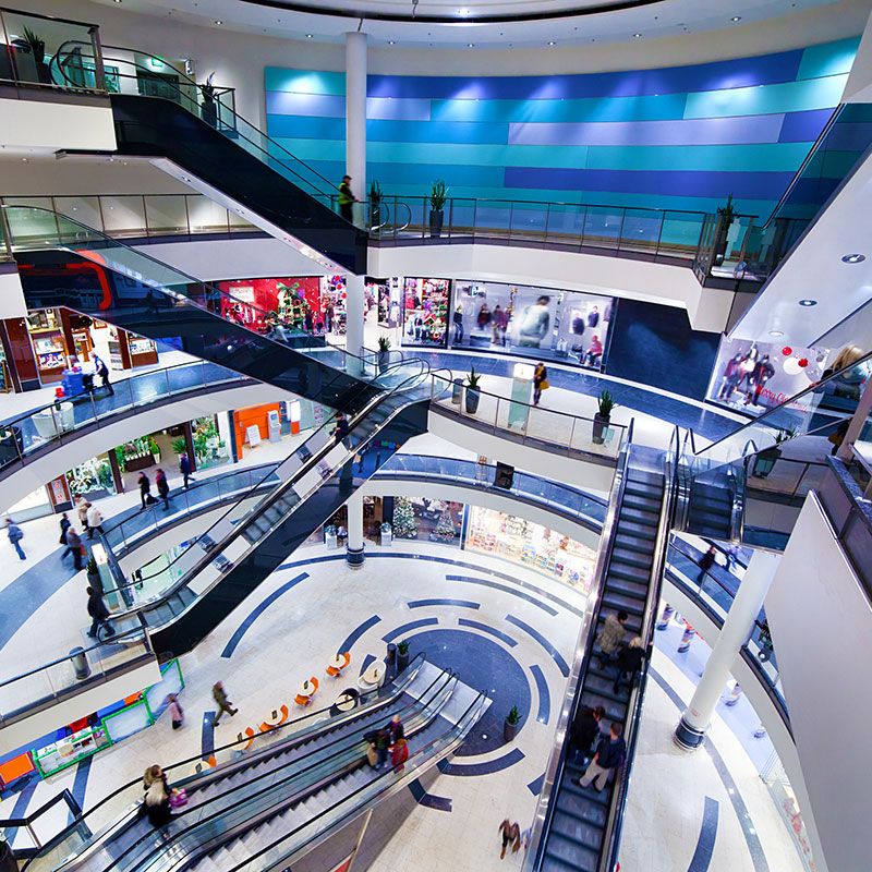 A big shopping mall with six escalators, and peopel walking in the mall. 